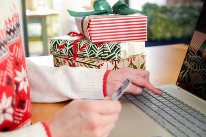 A woman with wrapped Christmas presents beside her types her credit card information into a laptop.