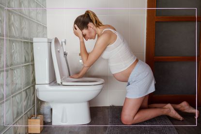 pregnant woman holding her head over the toilet struggling with morning sickness