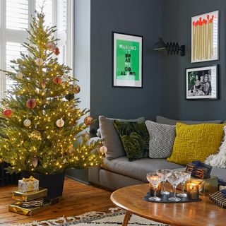 Navy blue living room with real Christmas tree, presents and grey sofa