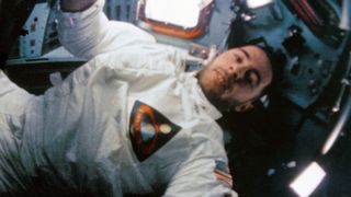 a man in a white flight suit is seen inside a space capsule