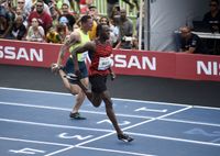 Usain Bolt runs on a track while spectators watch. Another man runs close behind him.