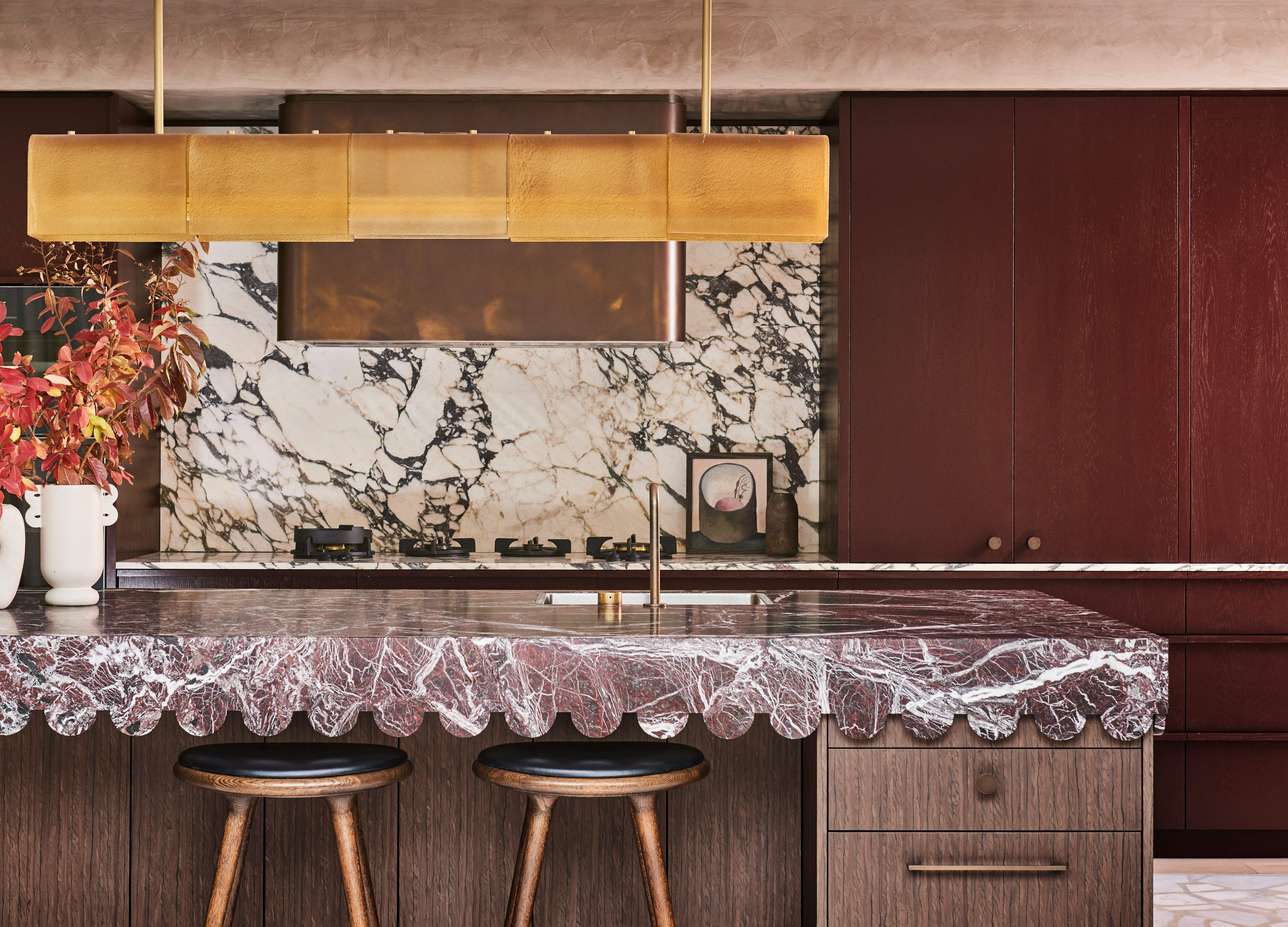 A kitchen with a burgundy countertop, a gold-finished pendant light, and burgundy kitchen cabinets