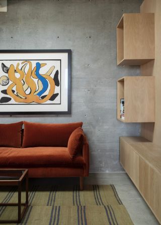 Living room with deep terracotta velvet sofa against grey concrete wall