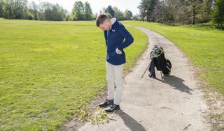 A golfer looks down at their ball on a path