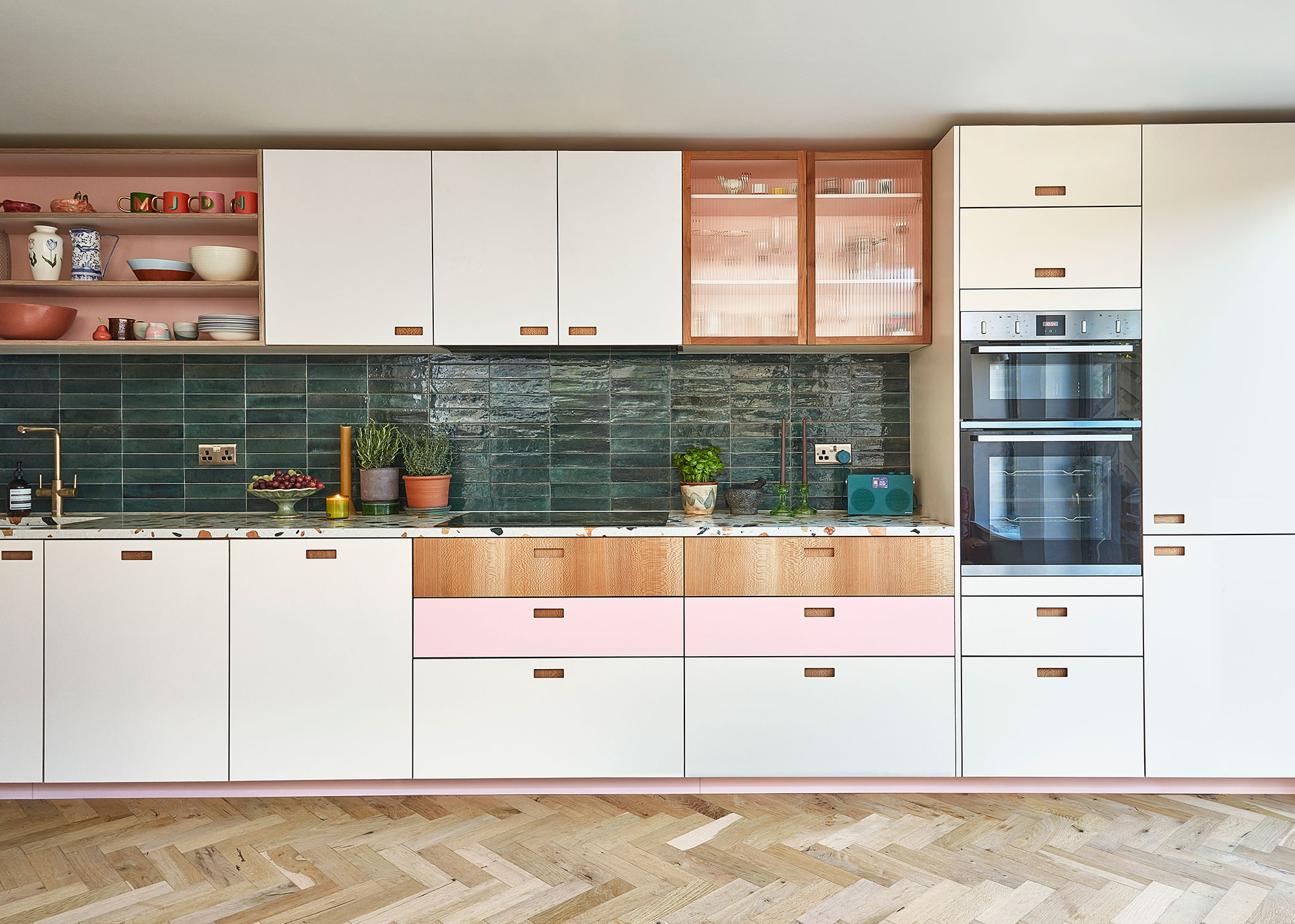 pink and white kitchen with drawers and green tiled splashback