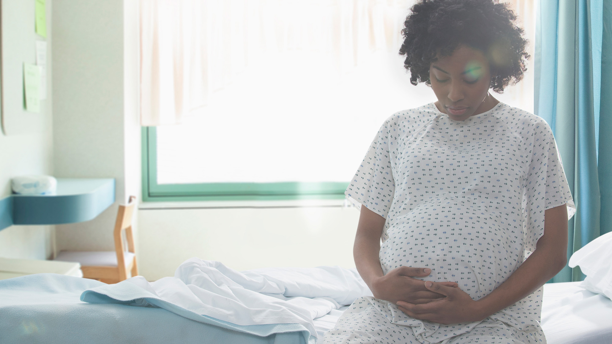 A woman wearing a hospital gown holds her pregnant stomach.