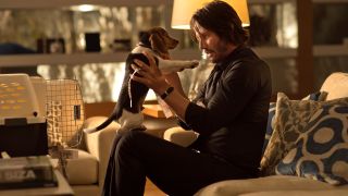 Keanu Reeves holds a beagle puppy while sitting on the couch in John Wick.