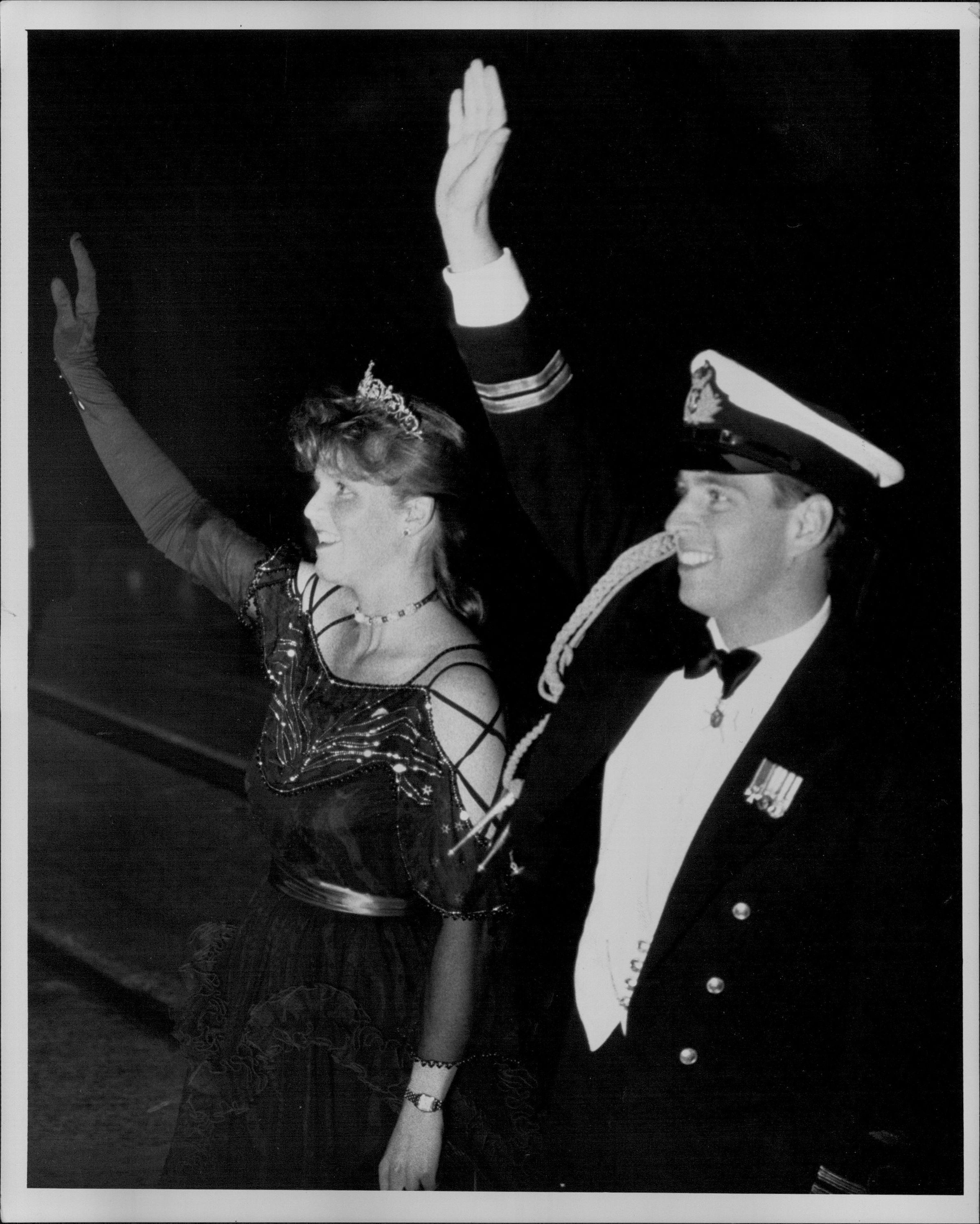 Sarah Ferguson wearing a tiara and evening dress waving next to Prince Andrew, in a naval uniform