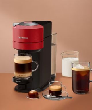 A Nespresso coffee maker surrounded by mugs of coffee against a terracotta background.