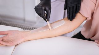 professional applying hair removal cream to a woman's arm