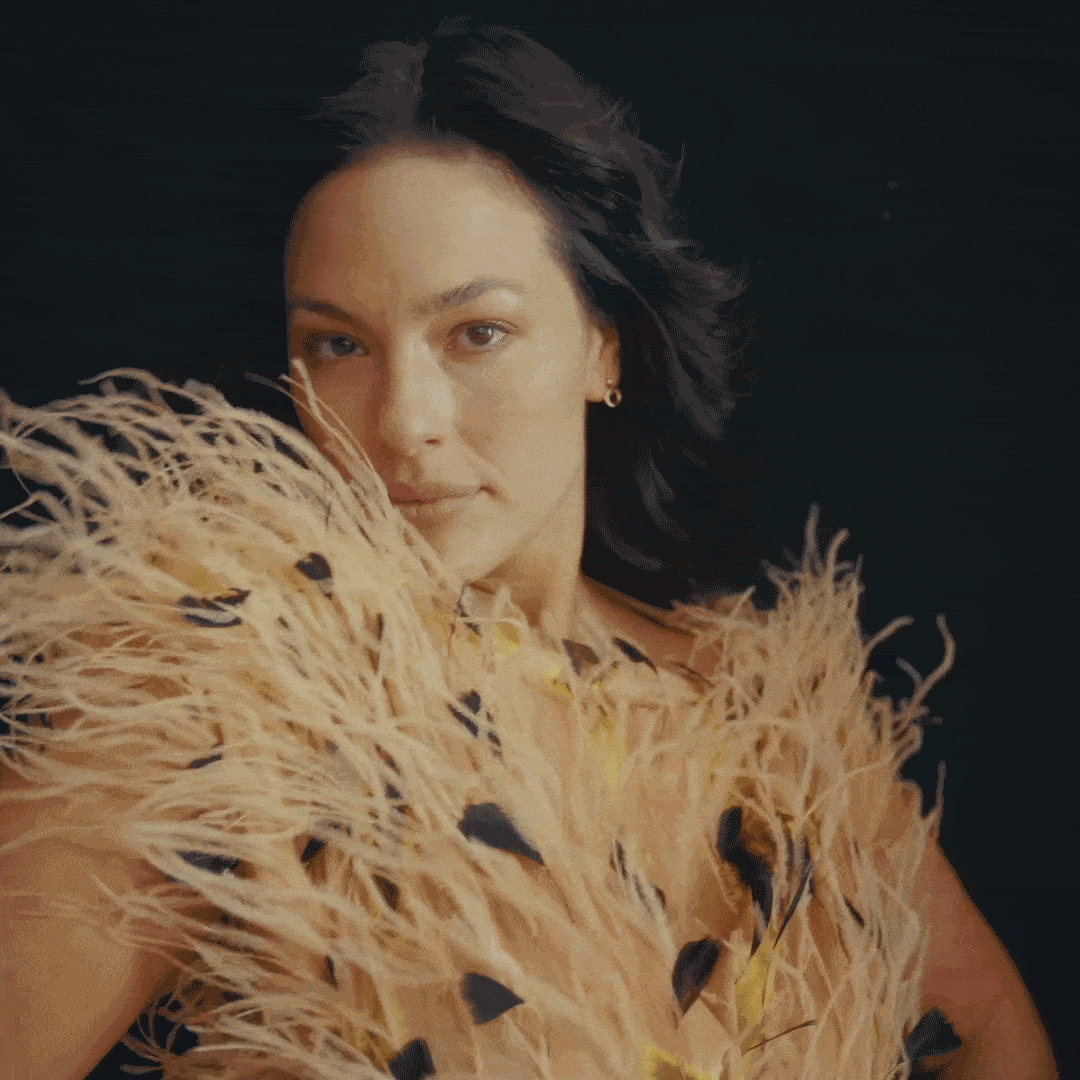 a woman in a tan feathered dress in a video gif