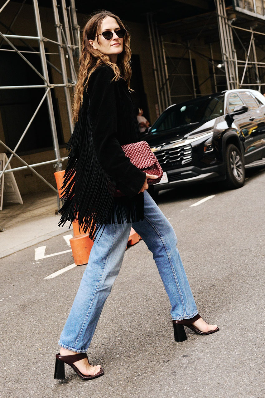 A woman wearing a black coat, blue jeans, and open-toe heels