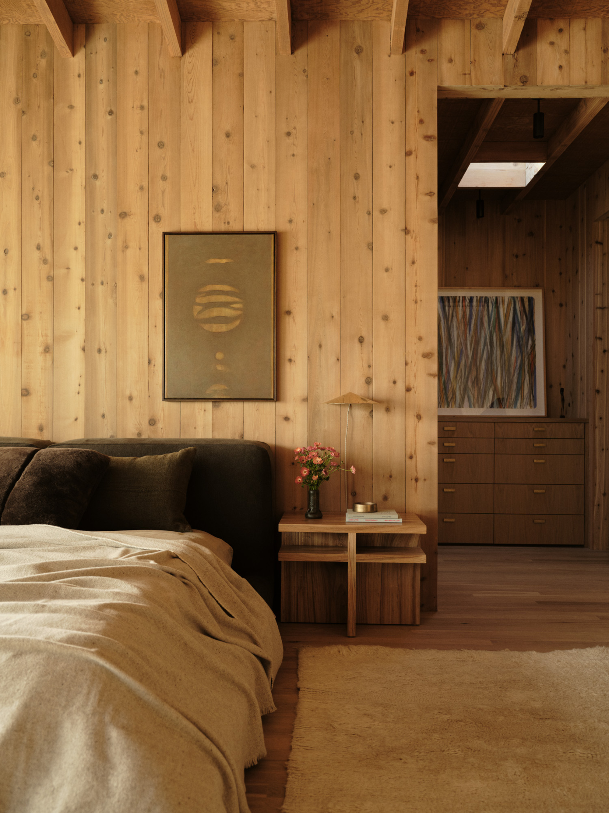 Image of a high-pile white rug in a bedroom that is drenched in natural wood panelling. The bed is a dark green upholstered frame with cream bedding.