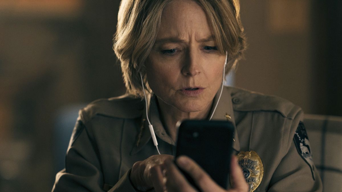 Jodie Foster in True Detective Night Country, looking concerned while using her smartphone