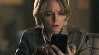 Jodie Foster in True Detective Night Country, looking concerned while using her smartphone