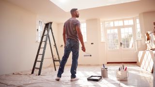 Man holding paint roller next to ladder in empty room
