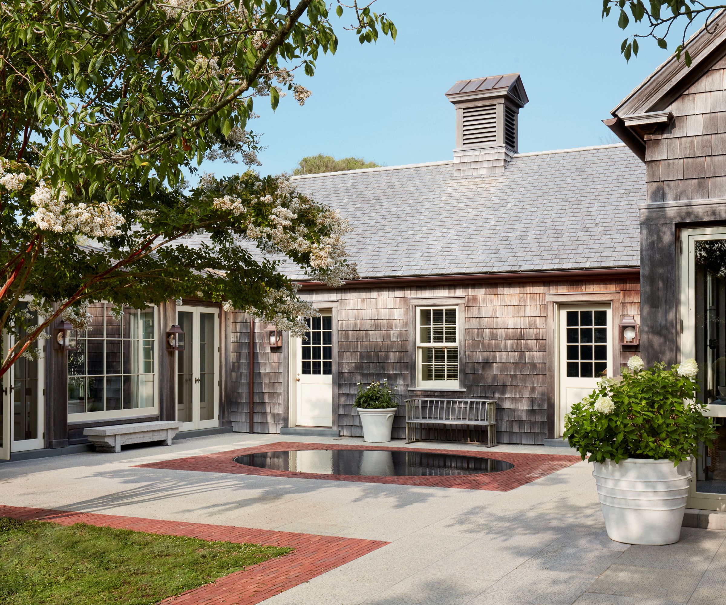 Shingle style home with white doors and windows, back porch with paved patio and bench and large potted plants in white pots