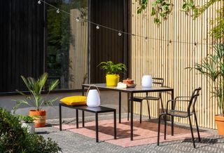 Black metal outdoor patio furniture ideas in a scheme with wood slatted fencing and string lights.