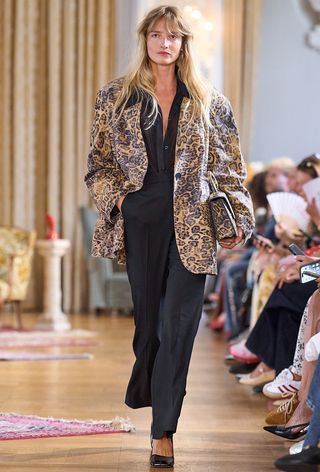 The leopard print coat trend is shown on the spring runway 2025 collection of Gestuz with a model walking wearing a leopard print oversized blazer over a black button-down shirt with black trousers and black pumps