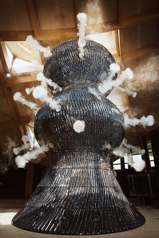 Close up view of Studio Swine’s dark coloured, curvy and textured sculpture with fog rings erupting from it