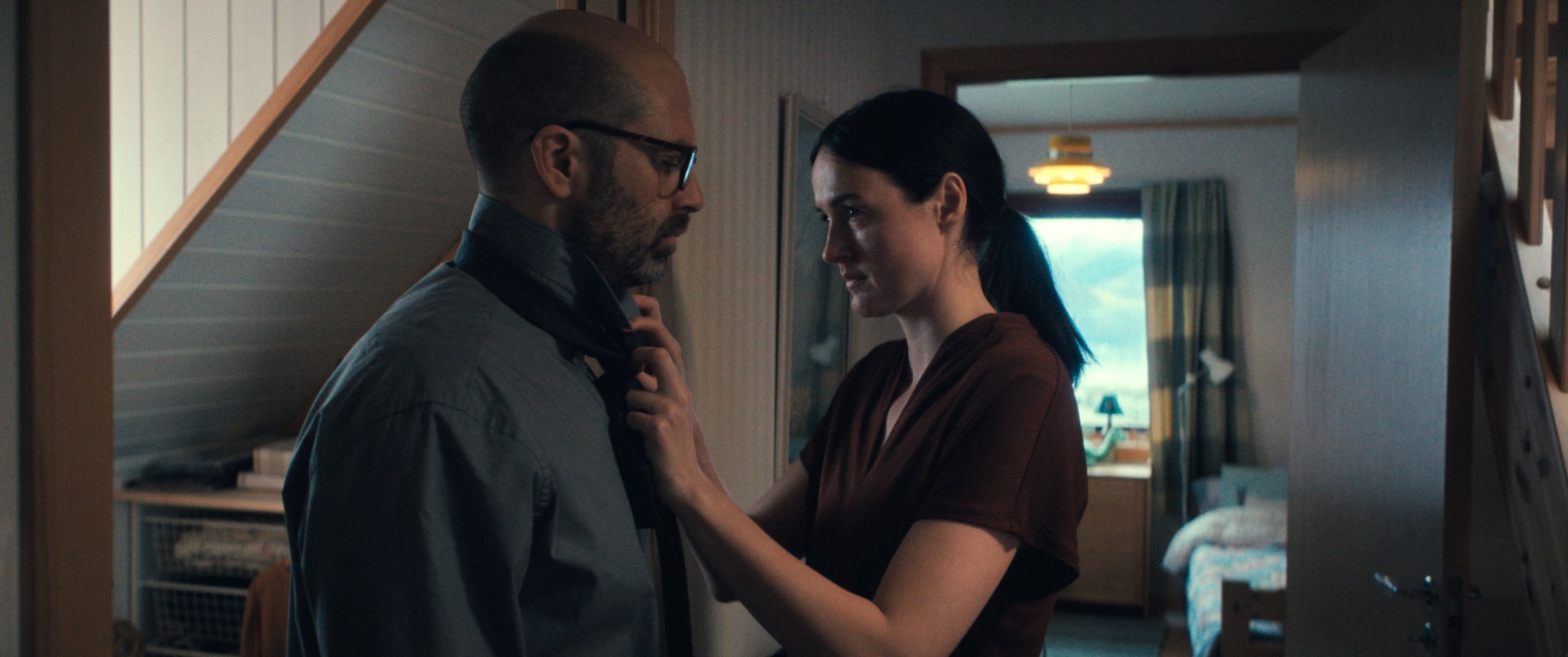 renate reinsve ties sebastian stan's tie in the hall of a norweigan home in a still from the movie fjord