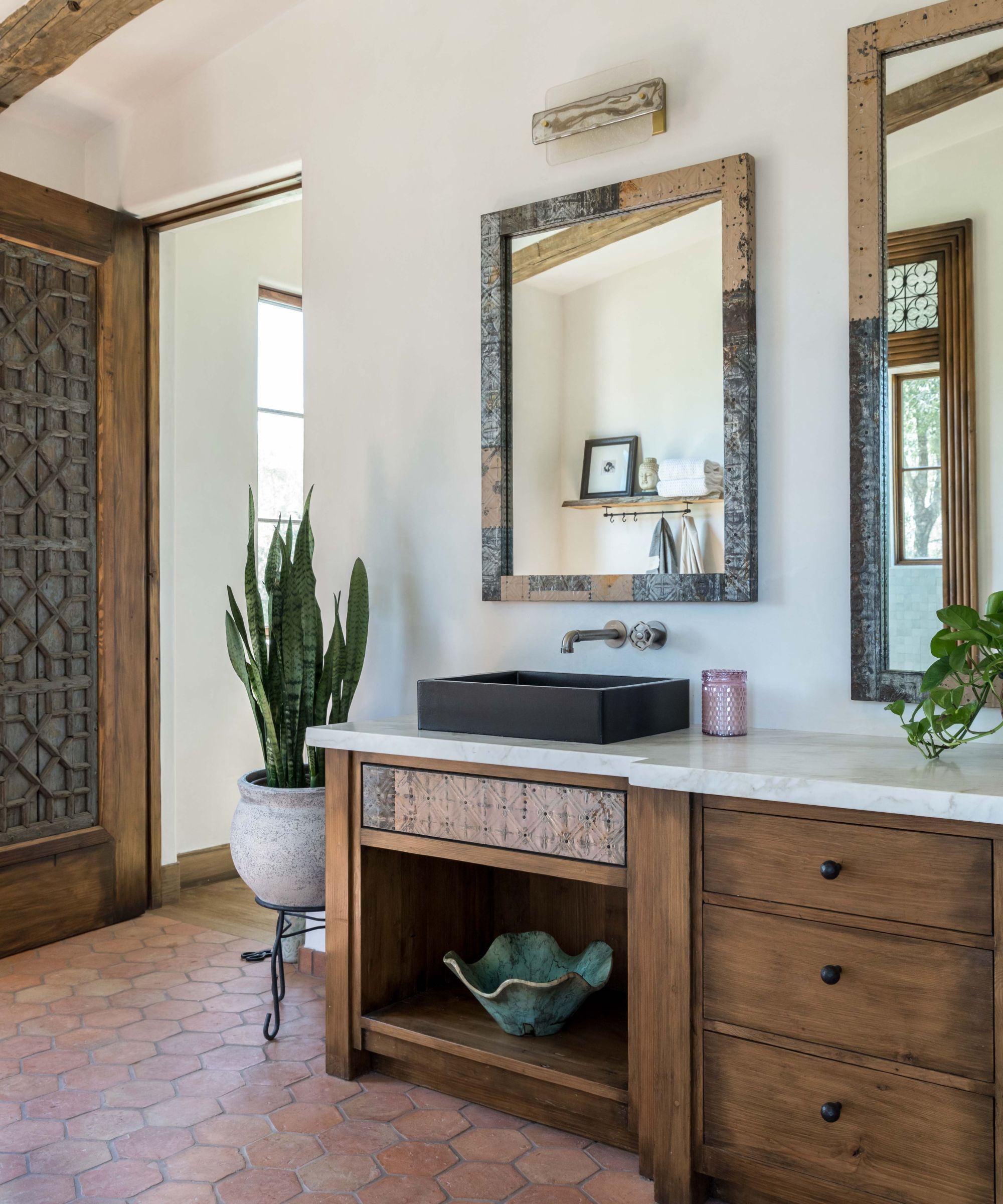 A Mediterranean bathroom with a wooden vanity, terracotta floor tiles, plaster walls, and potted plants