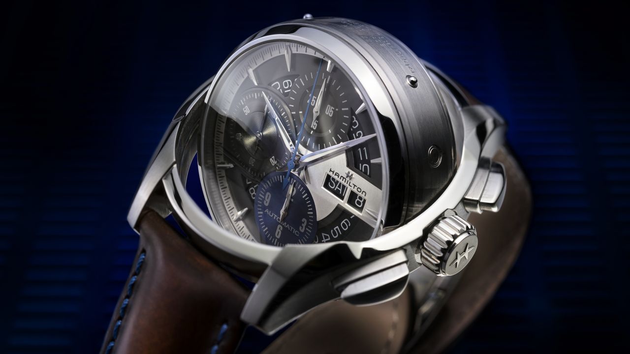 The Hamilton Jazzmaster Face-2-Face III watch mid rotation, with a brown leather strap on a blue background