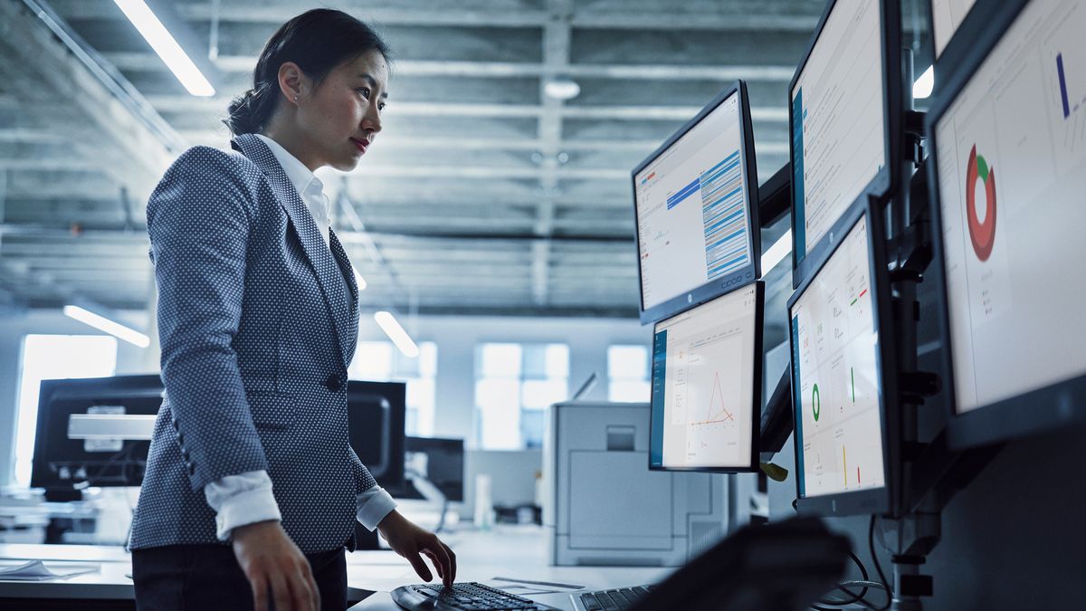 Standing woman looking at a bank of monitors showing graphs and written information