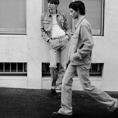 A black and white image of two people walking on the street wearing denim