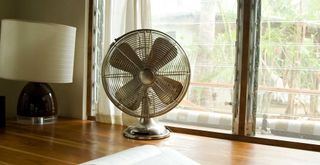 oscillating fan on a desk in front of a window to show a fan hack to make the room feel cooler