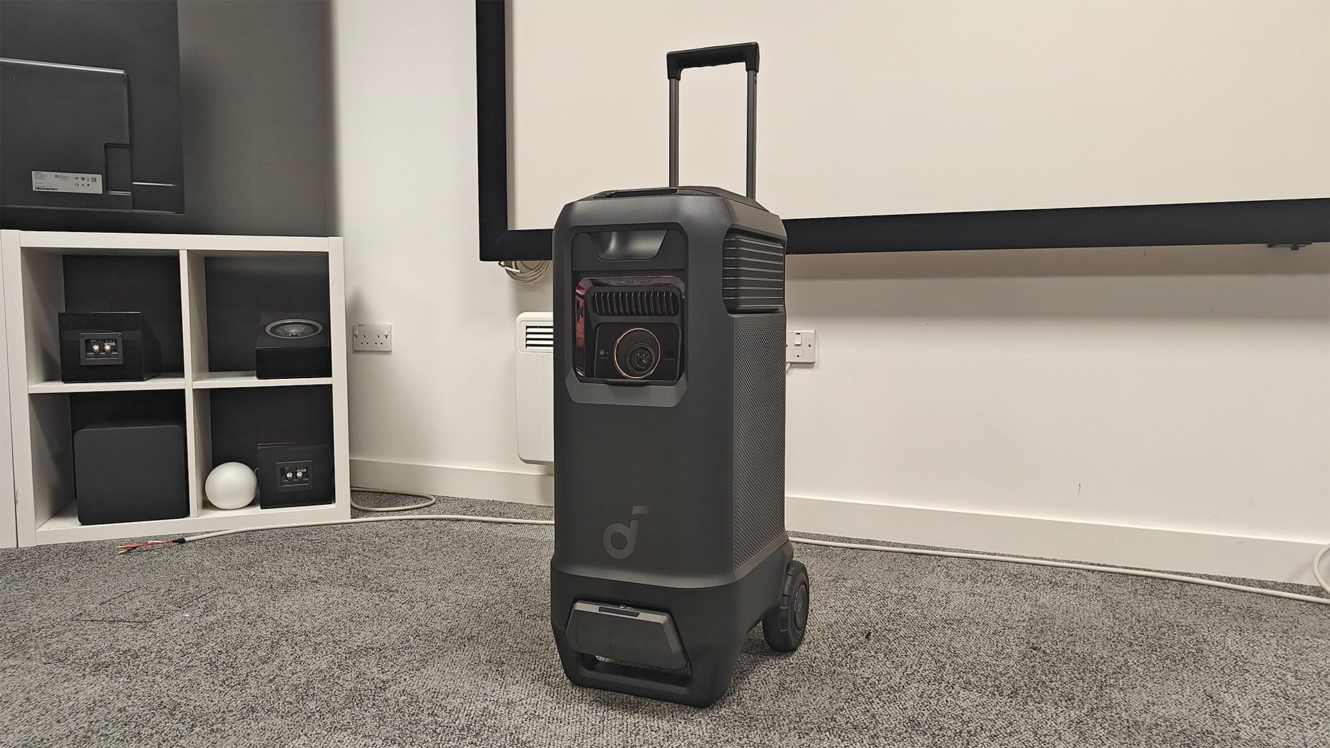 Soundcore Nebula X1 Pro home cinema projector on grey carpet in corner of test room with pull along handle extended