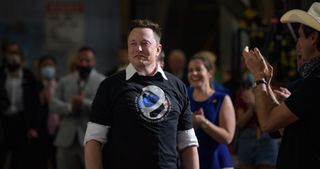 a man in a black t-shirt smiles while a crowd around him applauds