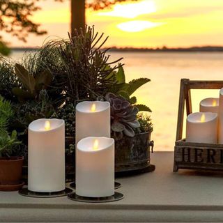 Three flameless outdoor candles on concrete with a blurred out ocean and a sunset in the background.