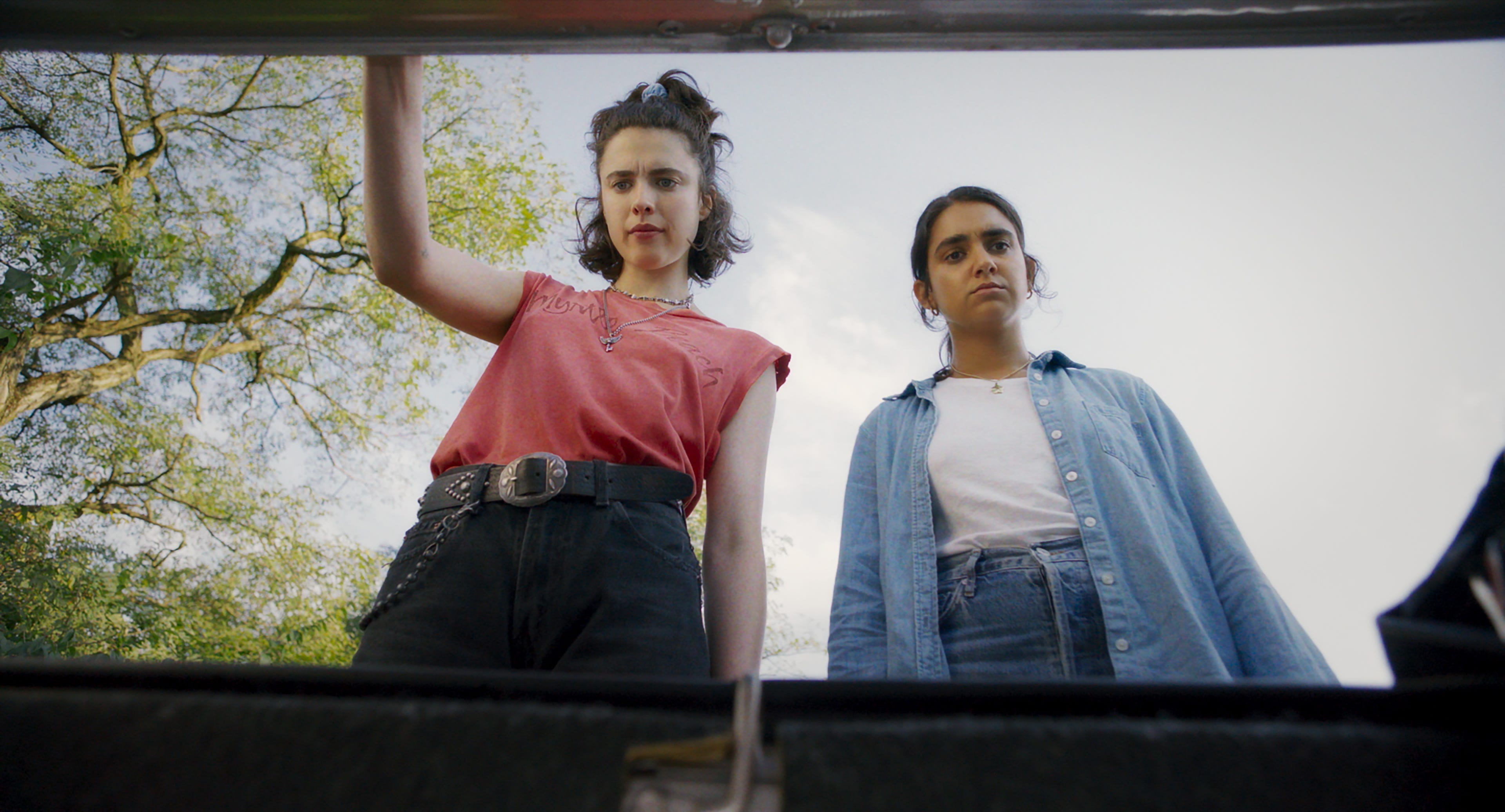 seen from the pov of a car trunk, a woman (margaret qualley) lifts the trunk's hood while another (geraldine Viswanathan) stands next to her