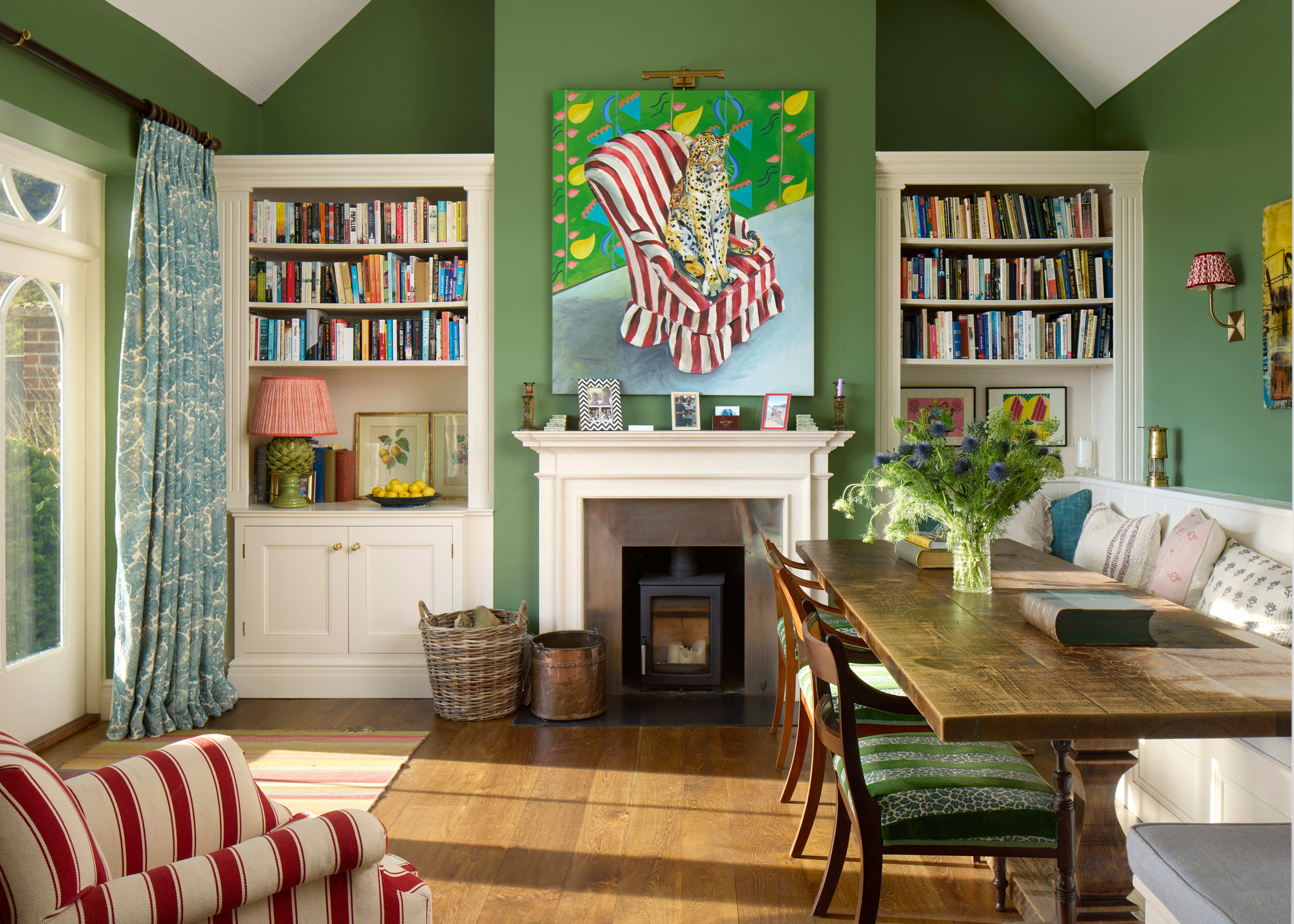 banquette seating with timber dining table in room painted green with fireplace