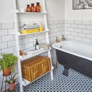 White batroom with grey bath tub and white ladder shelf with accessories
