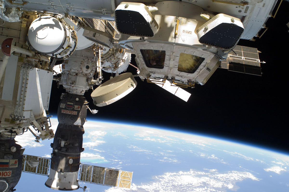 Backdropped by Earth&#039;s horizon and the blackness of space, the Cupola of the International Space Station and a docked Russian Progress spacecraft are featured in this image photographed by an Expedition 26 crew member while space shuttle Discovery (STS-13