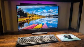 ASUS ROG Aura Monitor Light Bar emitting RGB lighting behind a monitor while shining LED white light on a keyboard and mouse. 