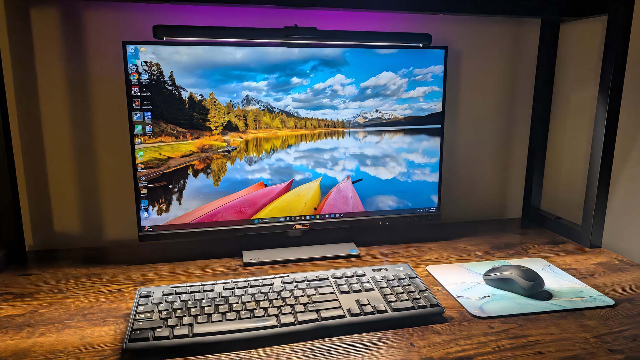 ASUS ROG Aura Monitor Light Bar emitting RGB lighting behind a monitor while shining LED white light on a keyboard and mouse. 
