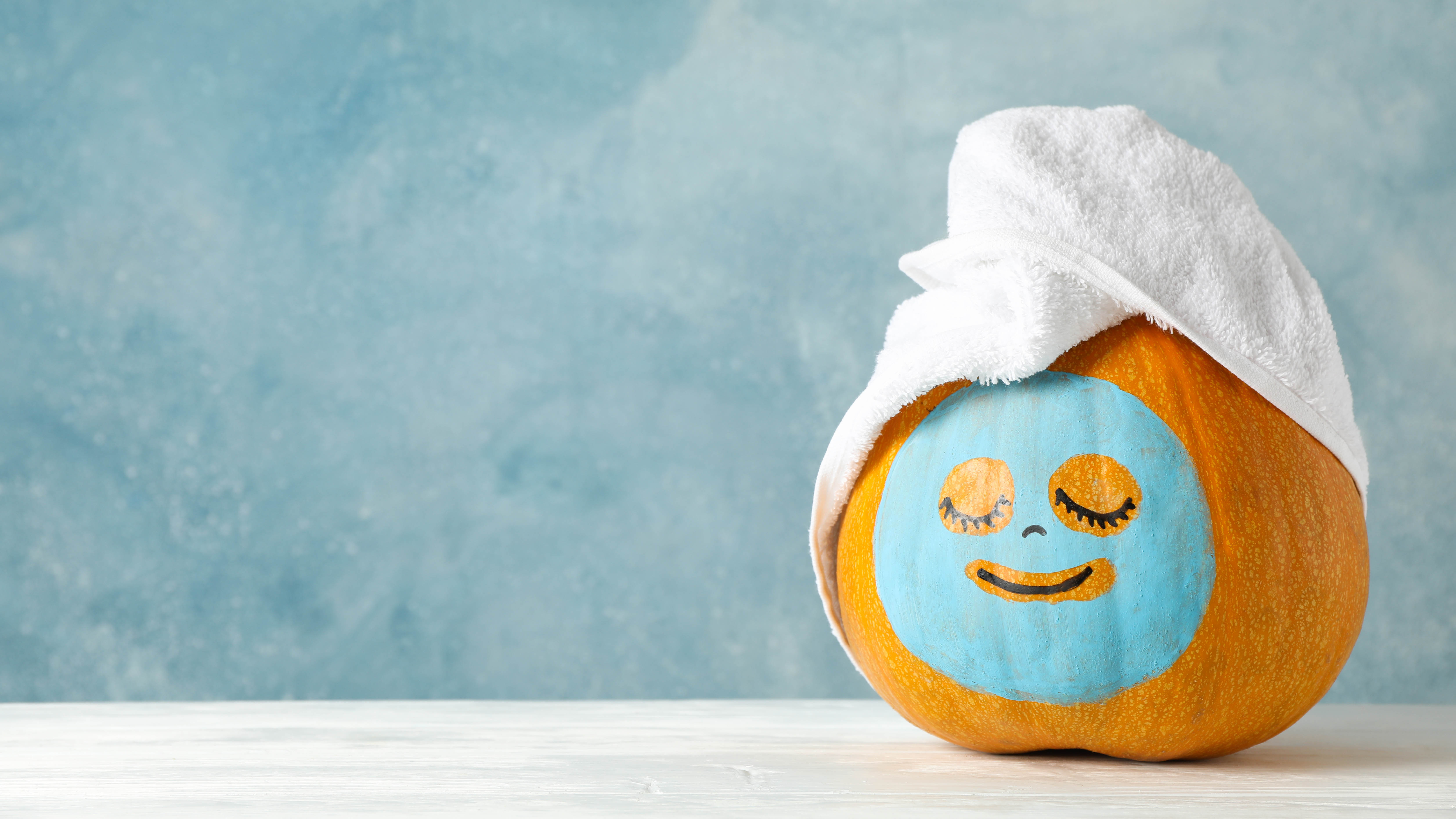 A pumpkin with a face mask drawn on wearing a towel on top