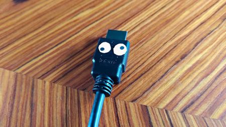 HDMI cable with cartoon eyes on woodgrain surface.