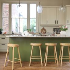 Open plan kitchen with green kitchen island and wooden stools.