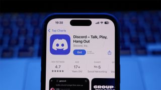iPhone displaying Discord app on the Apple App Store with a blurred laptop keyboard in the background