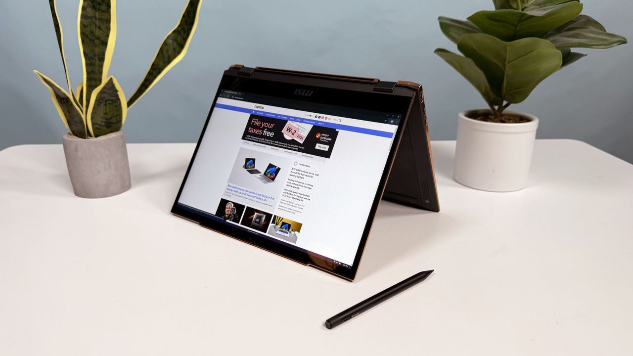 MSI Summit 13 AI+ Evo (A2VM) 2-in-1 laptop open in tent mode on a white table with a stylus resting in front of it and two plants behind it