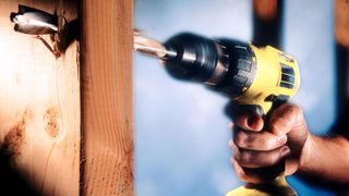 Cordless drill drilling into bare wood door