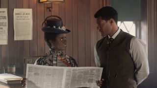 Denée Benton in a black hat and dress as Peggy holds a newspaper and talks to Sullivan Jones in a dark waistcoat as T Thomas Fortune in The Gilded Age season 2.