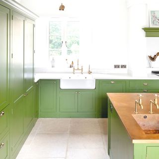 white walled kitchen with green cabinetry and limestone flooring