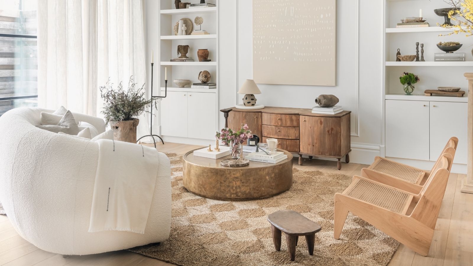A calm white living room with a white sofa and two wooden armchairs. On a woven rattan rug, with light wooden flooring. 