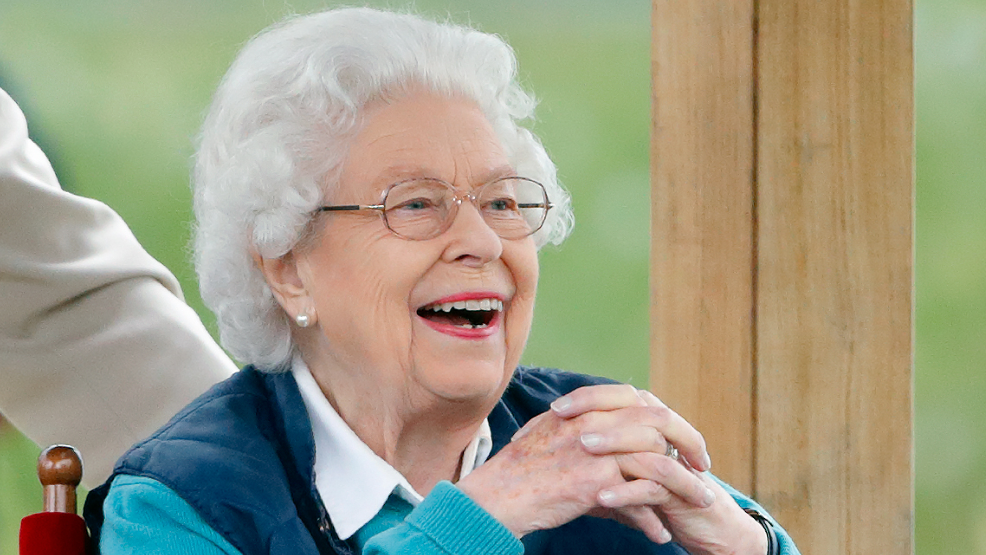 Queen Elizabeth wearing a blue vest and sweater smiling