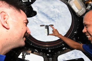 NASA astronauts Chris Williams holds his hand out, appearing to "hold" the Cygnus capsule from the ISS.